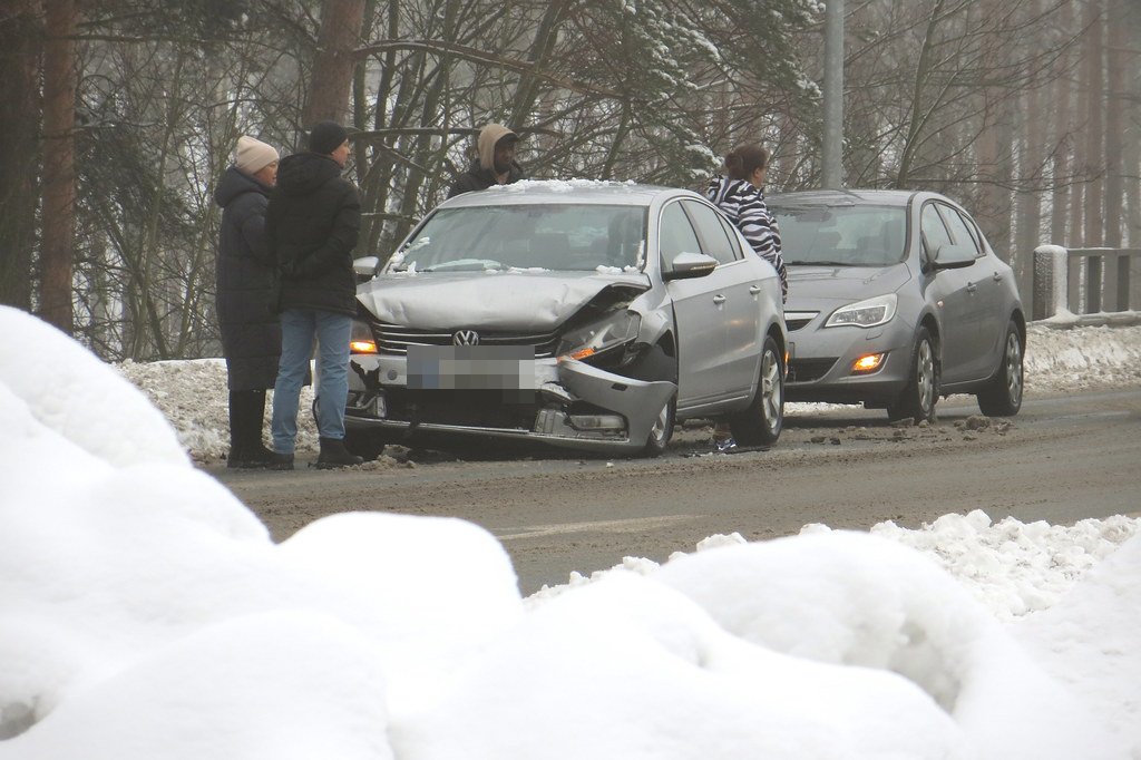 Two-car winter fender-bender with drivers standing roadside exchanging information (license plate pixelated)